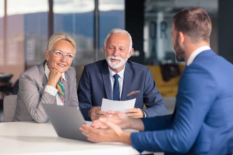 A couple reviews life insurance documents and a financial worksheet at a kitchen table.